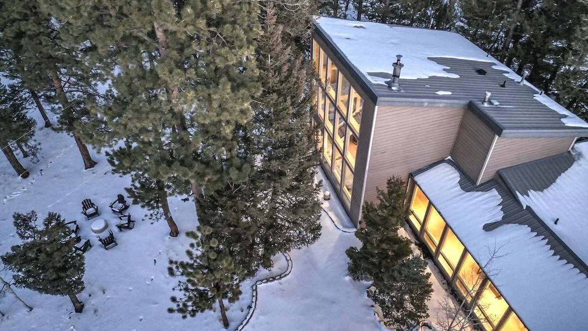 Aerial view of the snow-covered house and fire pit seating among pines