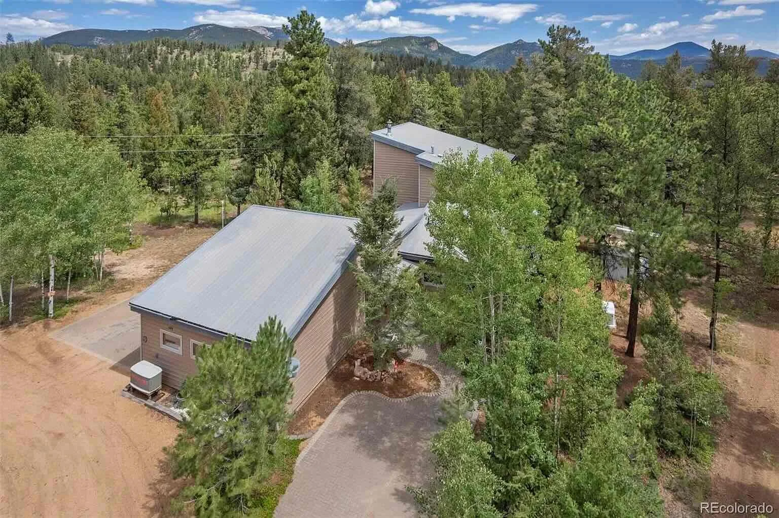 Aerial view of the house surrounded by trees with mountains behind