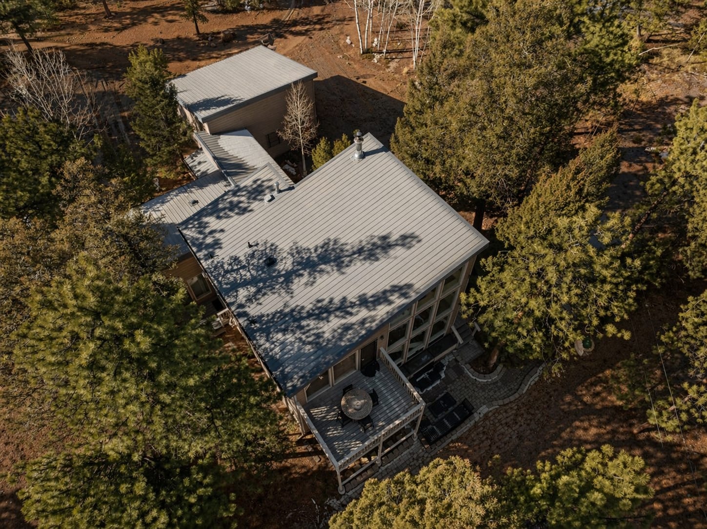 Top-down drone view of the house, decks and patio among pine trees