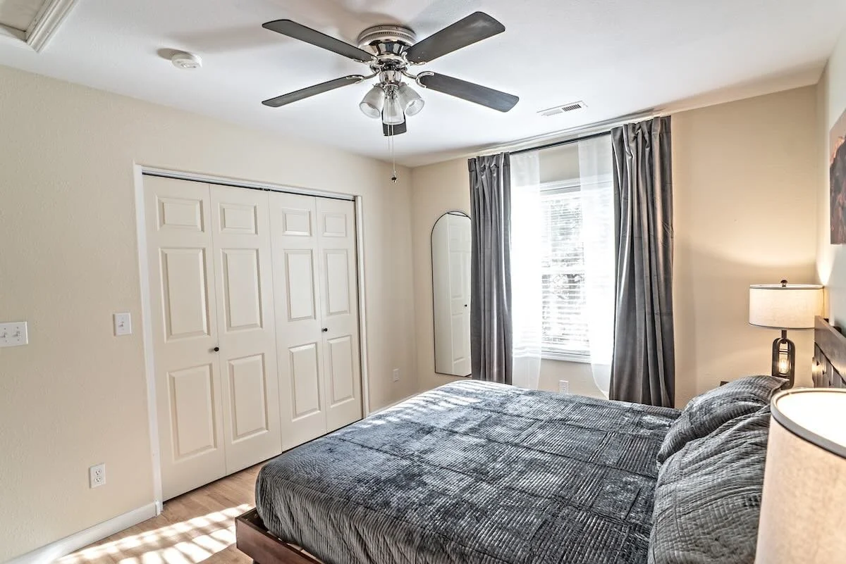 Second bedroom with curtained window, ceiling fan and a two-door closet