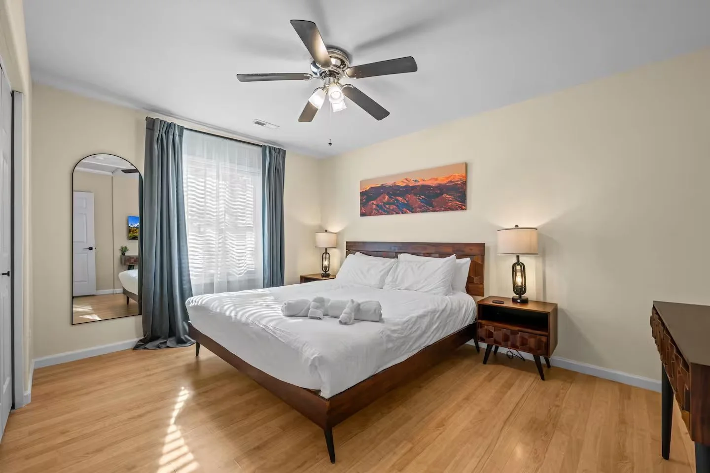 Second bedroom with wooden bed frame, arched mirror and window with blue curtains