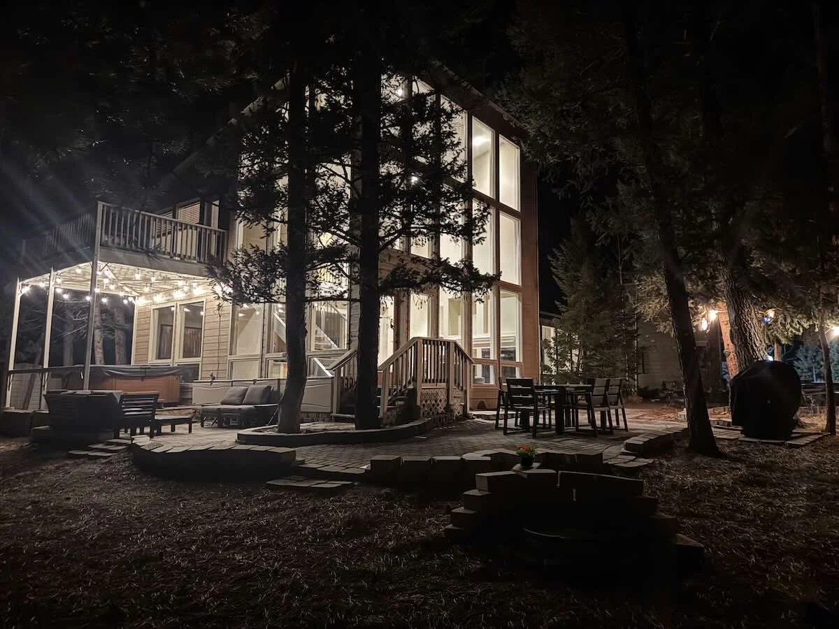 House at night with lit windows, deck furniture, string lights and grill
