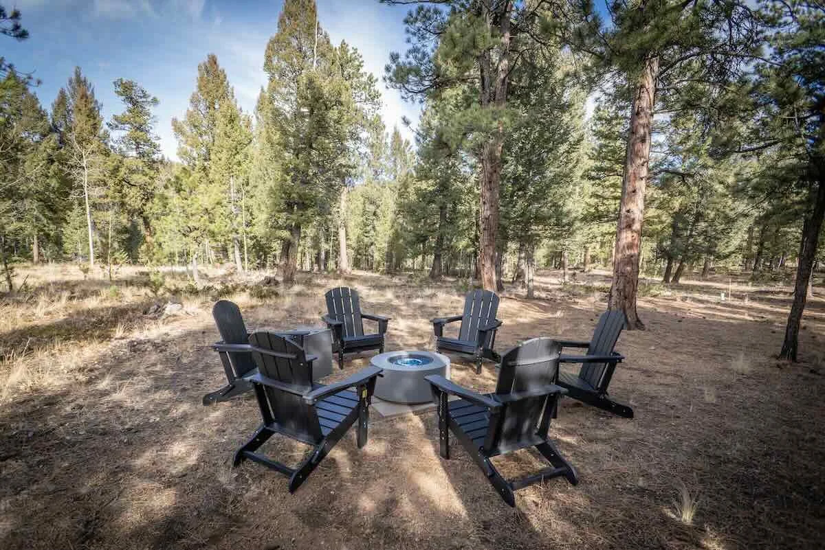 Six Adirondack chairs circling a metal fire pit in the trees