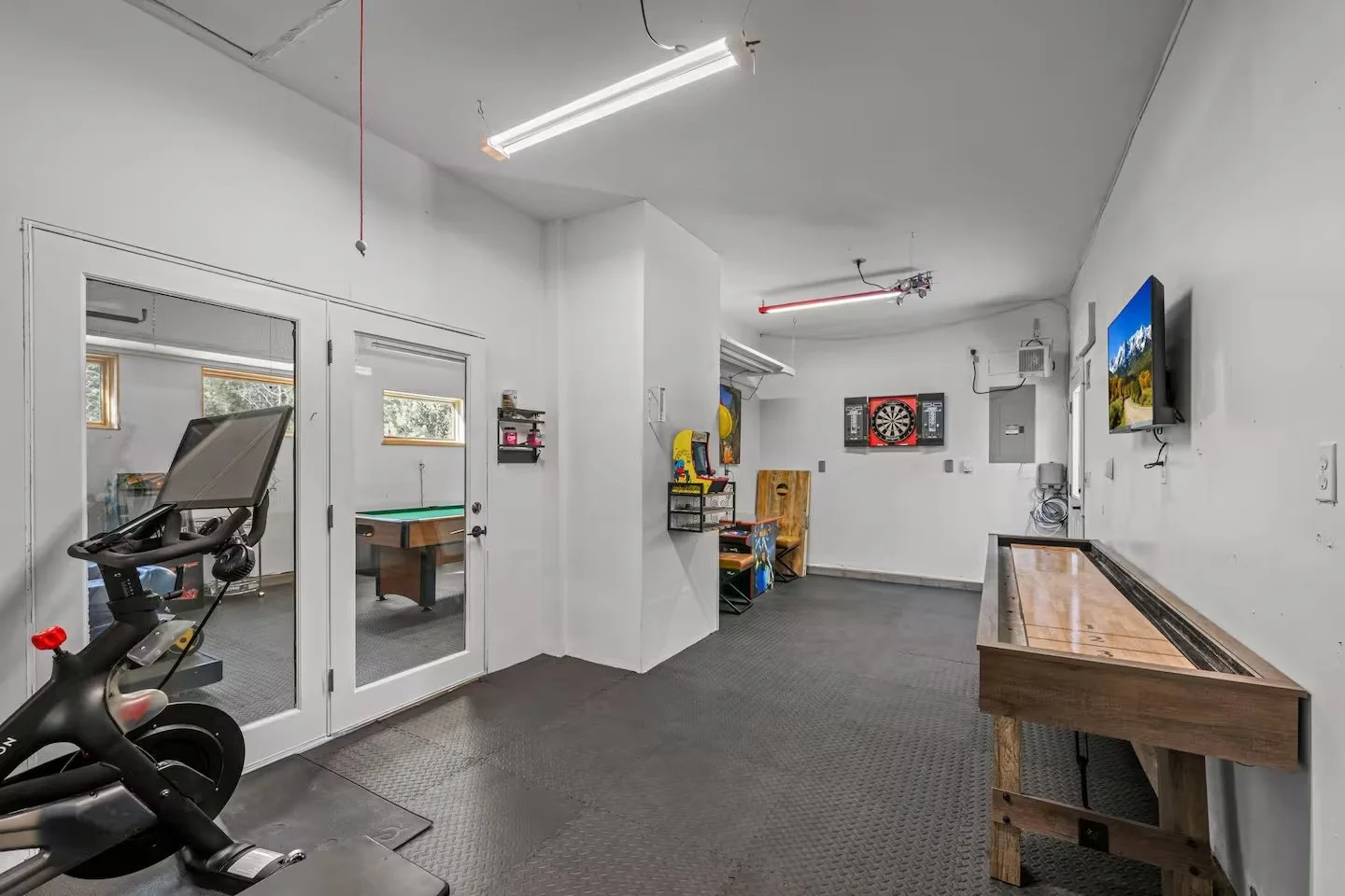 Recreation room with arcade cabinets, dartboard, TV and exercise bike