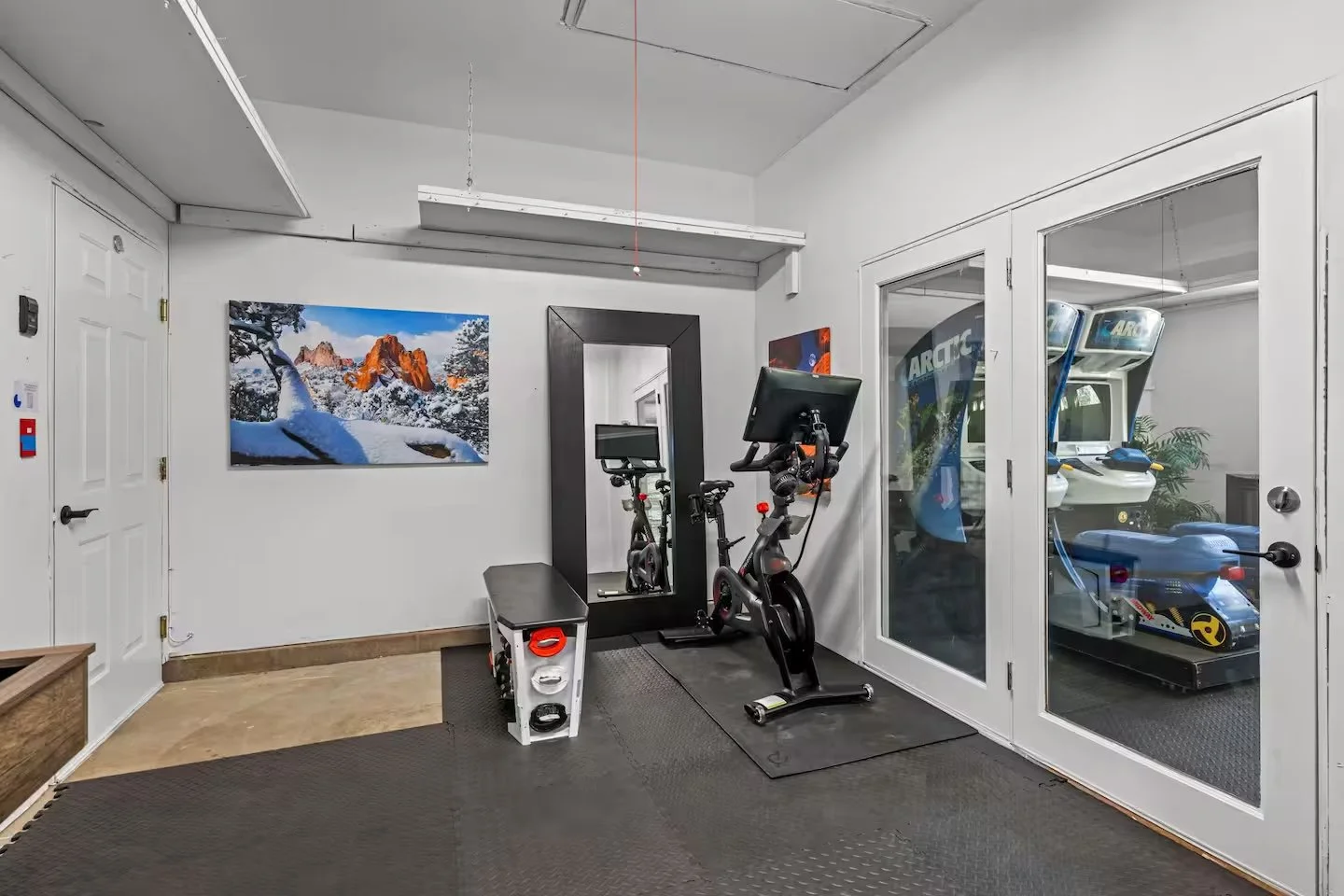 Gym area with bike and bench, arcade racing games visible behind a glass wall