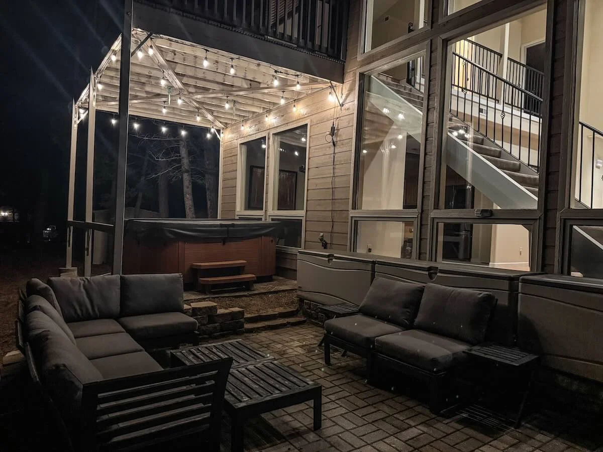 Patio at night with string lights, hot tub and lit windows