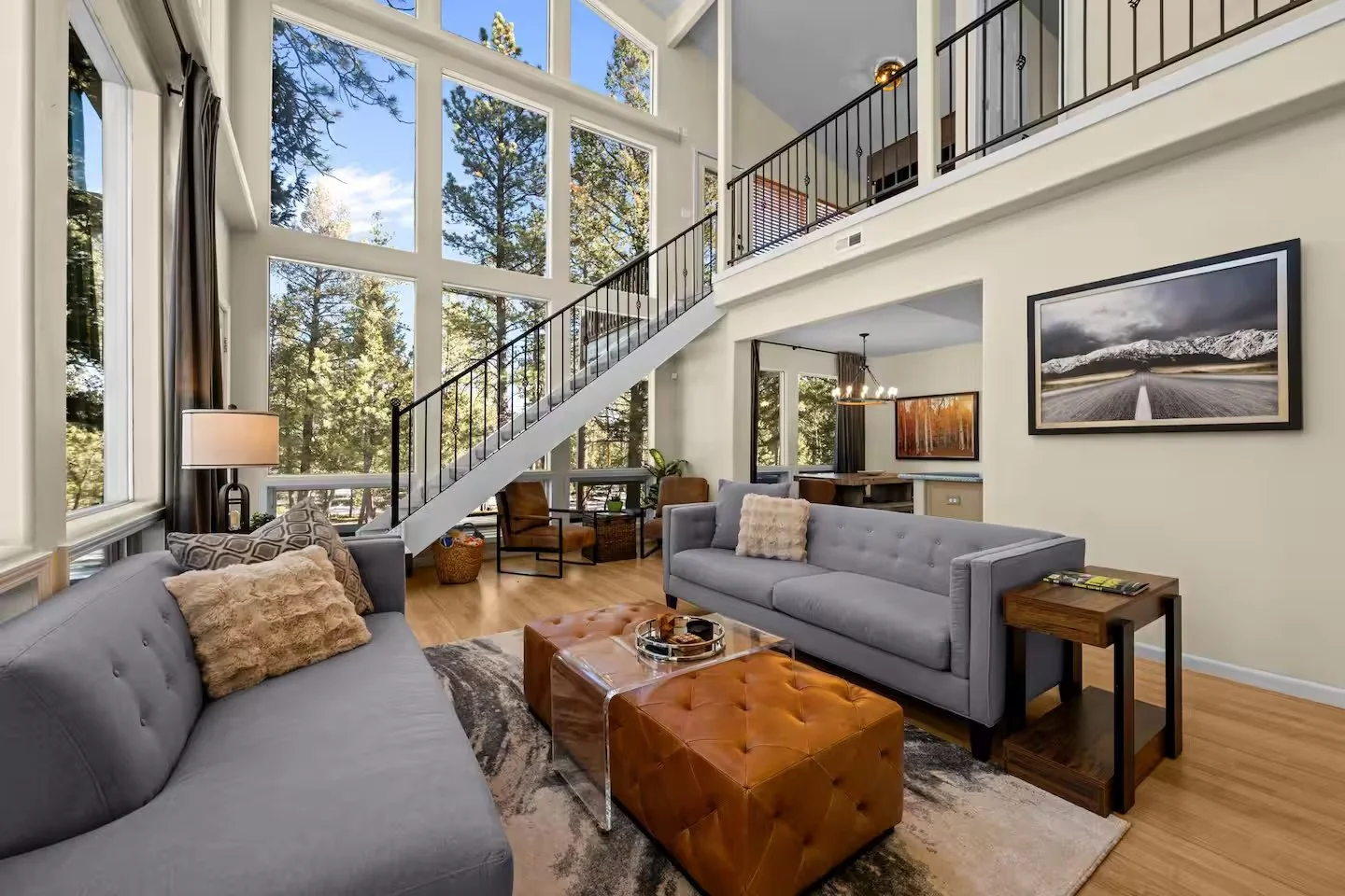 Living room with floor-to-ceiling windows showing forest, sofas and leather ottoman