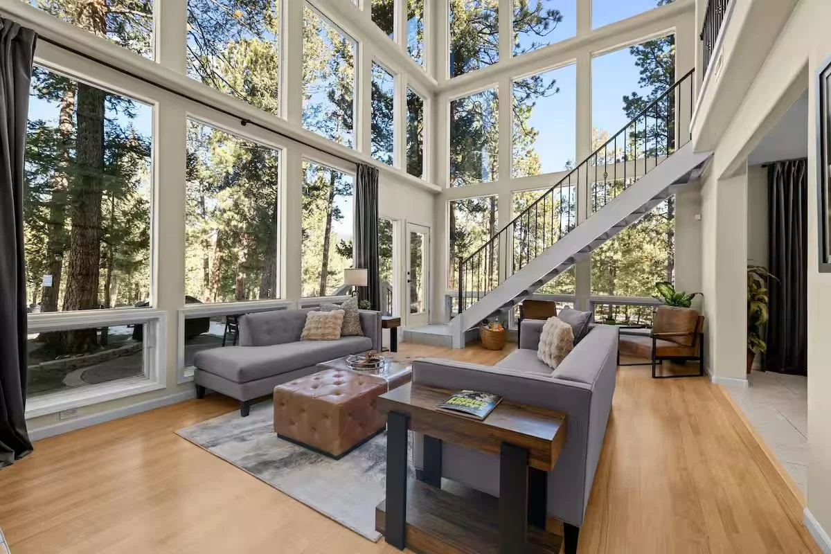 Bright living room with two-story windows, gray sofas, wooden table and staircase