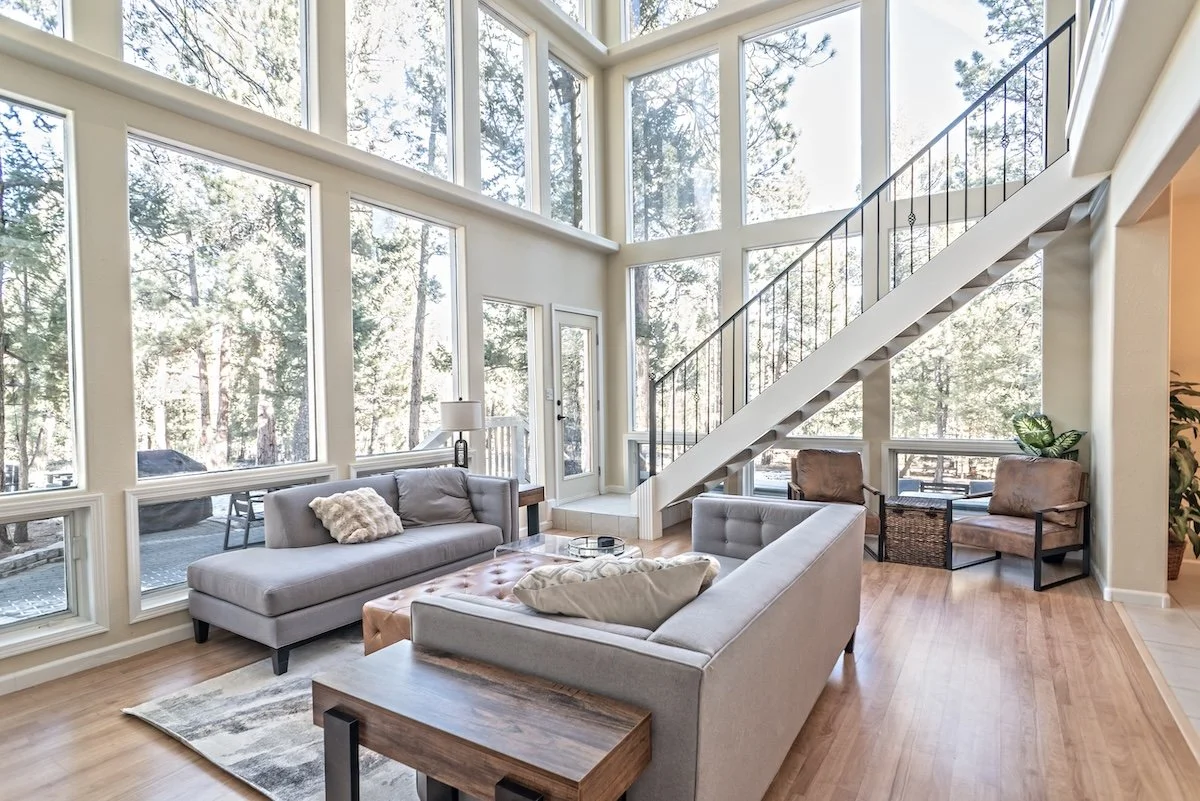Living room with a wall of windows, light gray sofas and a black-railed staircase