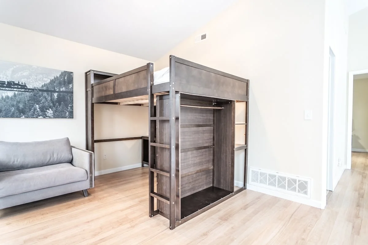 Loft bed with gray wood frame beside a sofa and window
