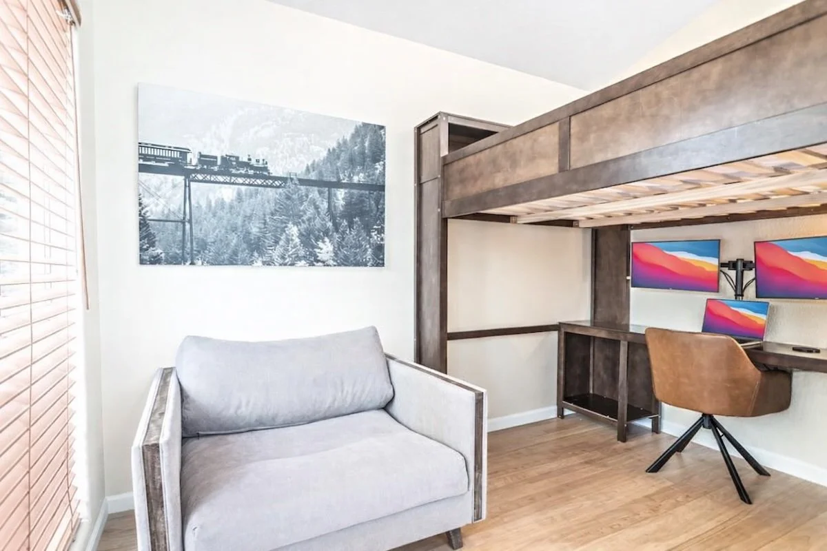 Loft workspace with three monitors, office chair and framed mountain photographs
