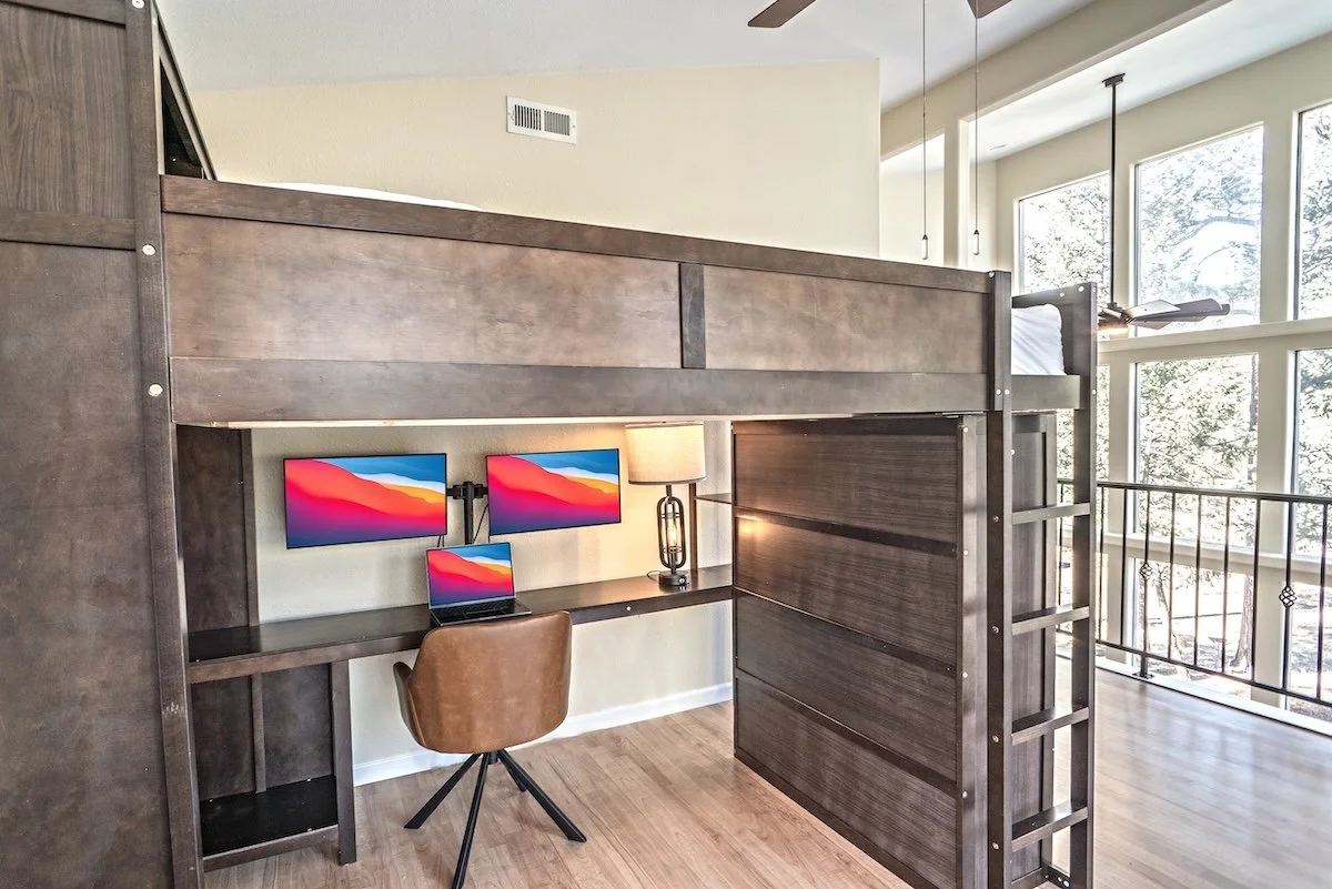 Loft bed with a workspace underneath holding two monitors, a laptop and a desk lamp