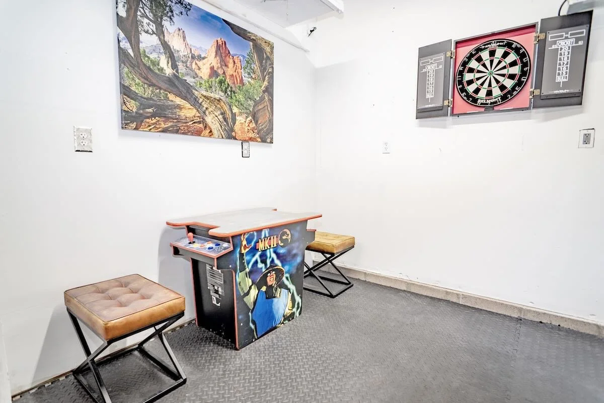 Dartboard, arcade cabinet and two stools on a rubber-floored room