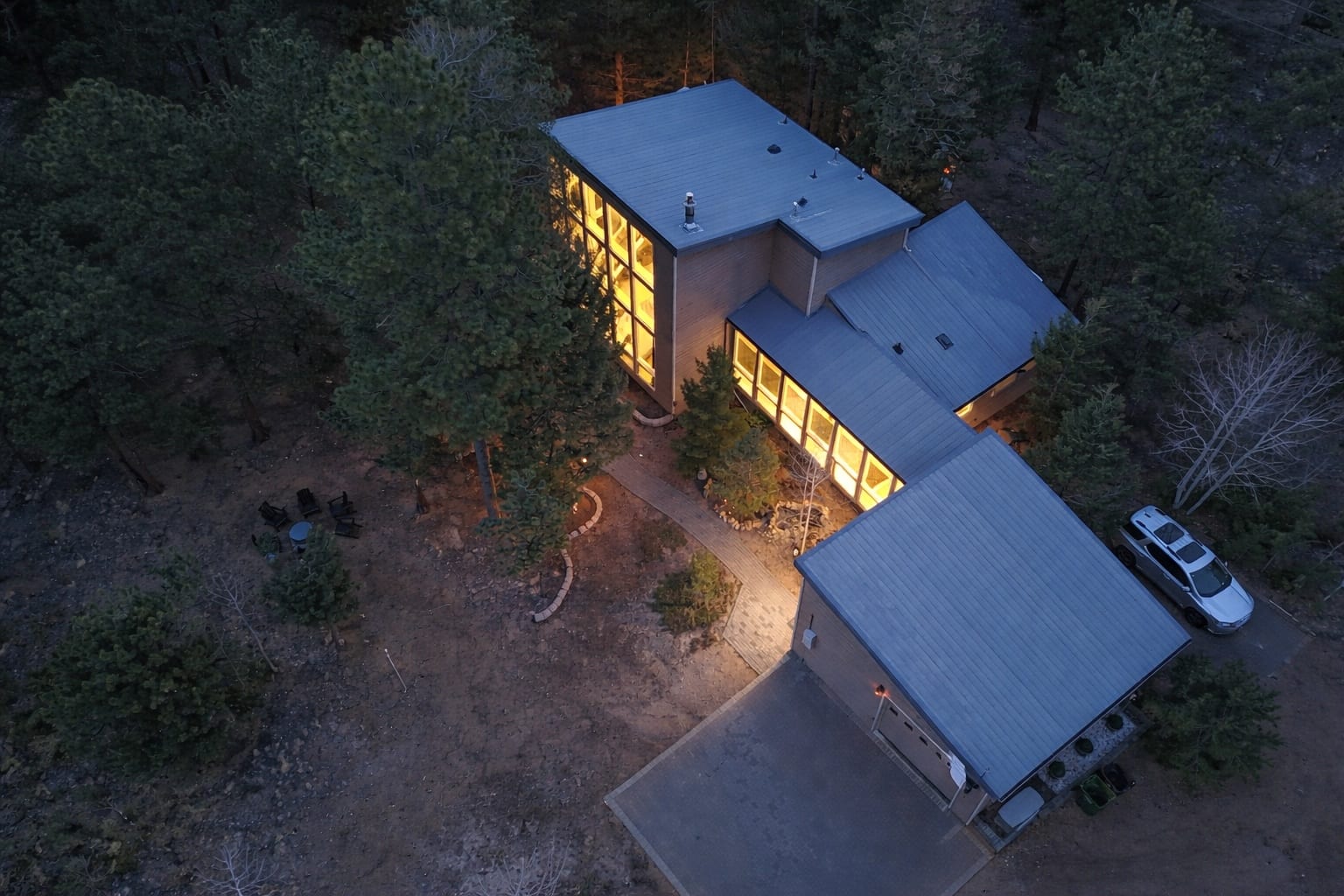 Aerial dusk view of The Stillwood Retreat illuminated among dense forest
