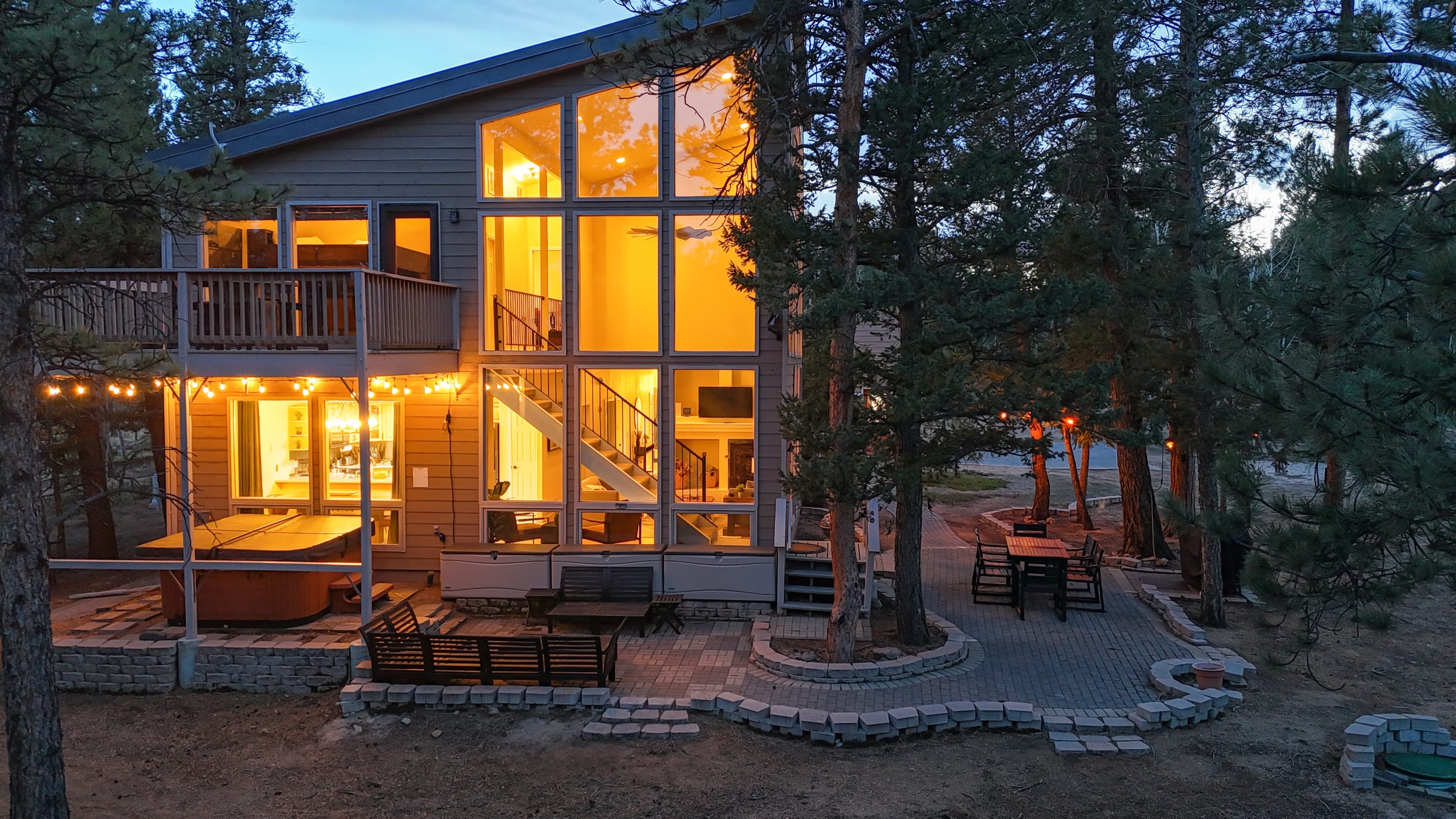 Two-story glass exterior glowing at dusk above the patio and hot tub