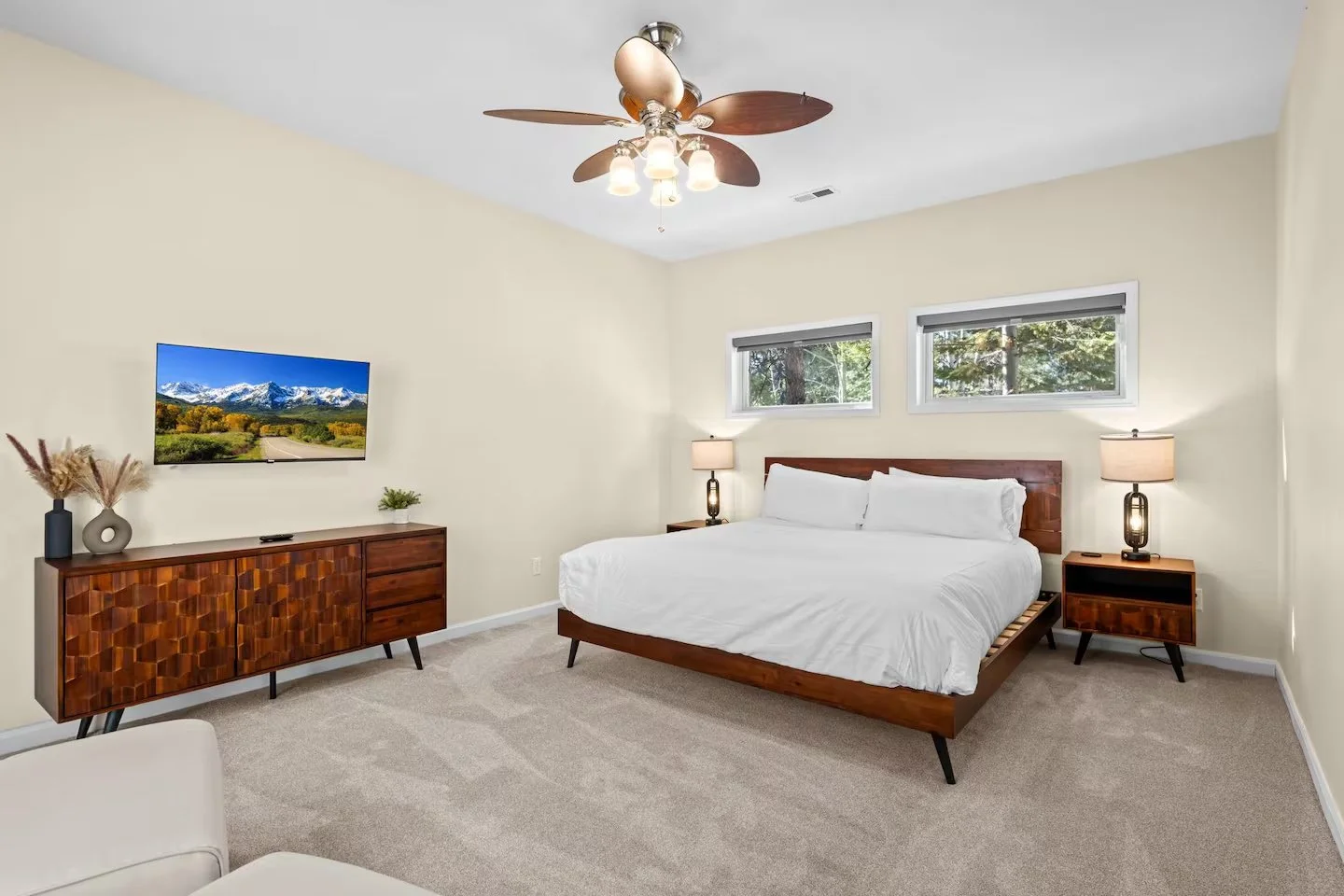 Bedroom with wooden bed frame, white bedding, two nightstands and a wall-mounted TV