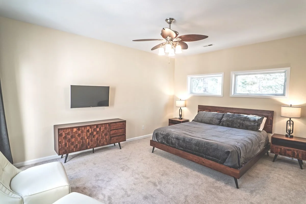 Primary bedroom with gray bedding, wooden furniture and two horizontal windows