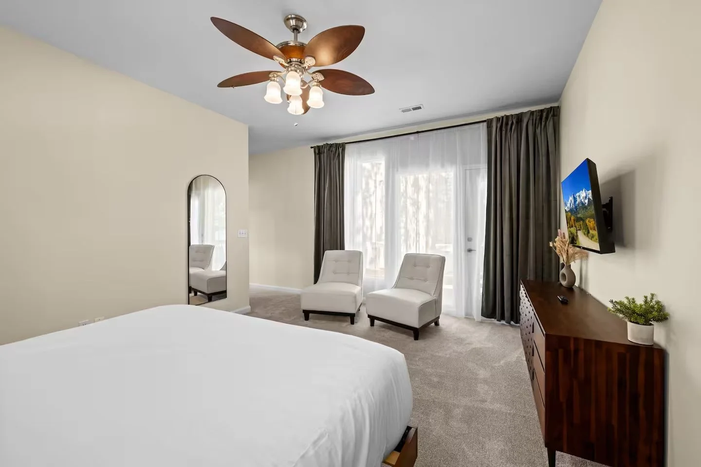 Bedroom with two chairs beside a sliding glass door and a dresser with TV
