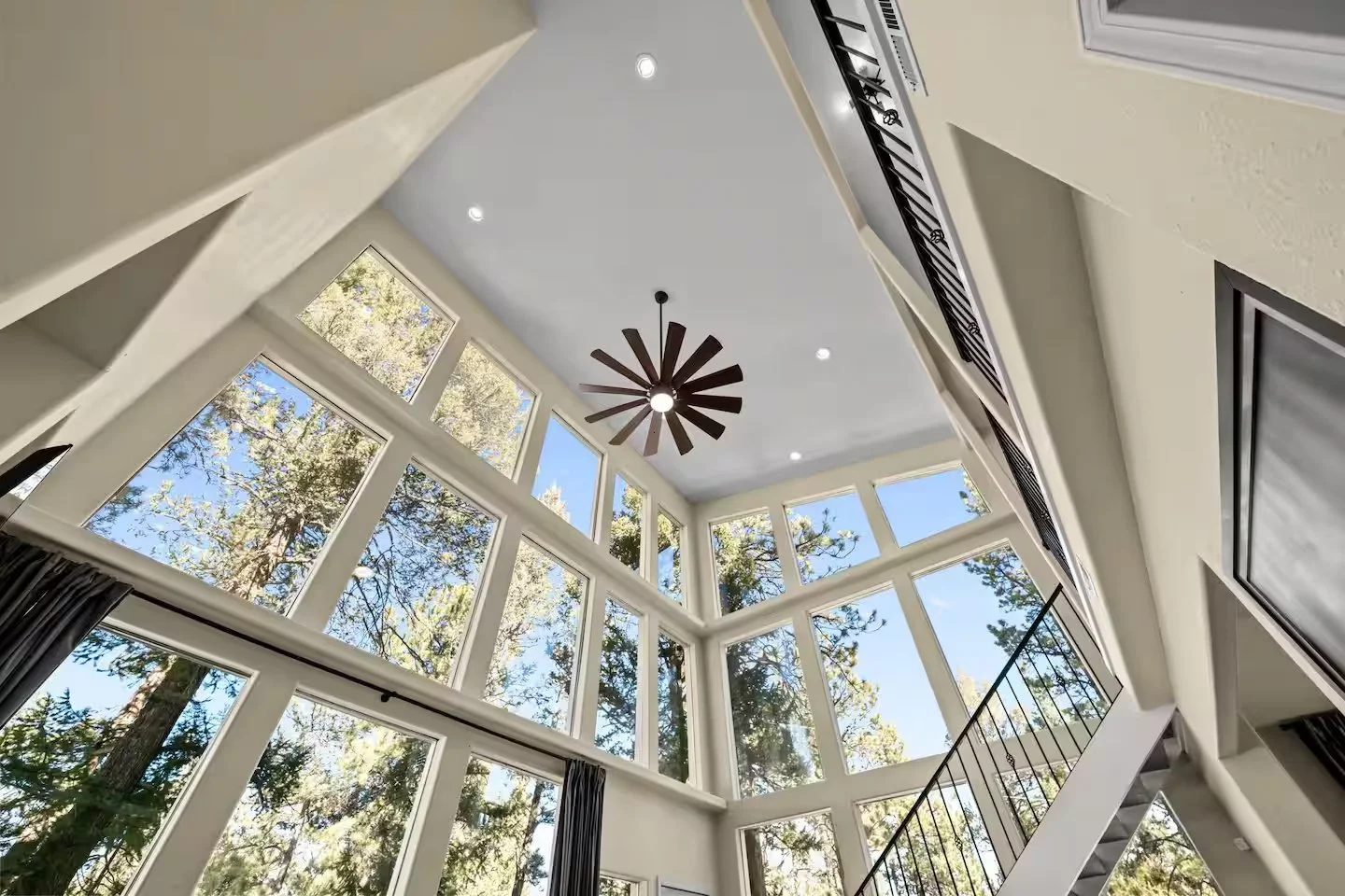 Floor-to-ceiling windows and black-railed staircase looking out to trees and sky